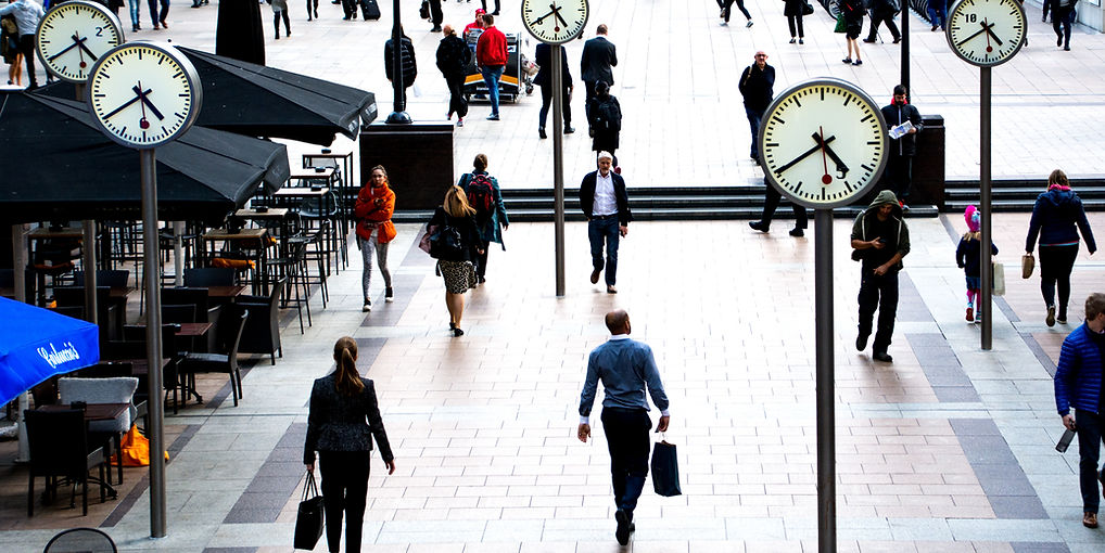 People in a busy city street beneath large clocks, mirroring the pace of life.